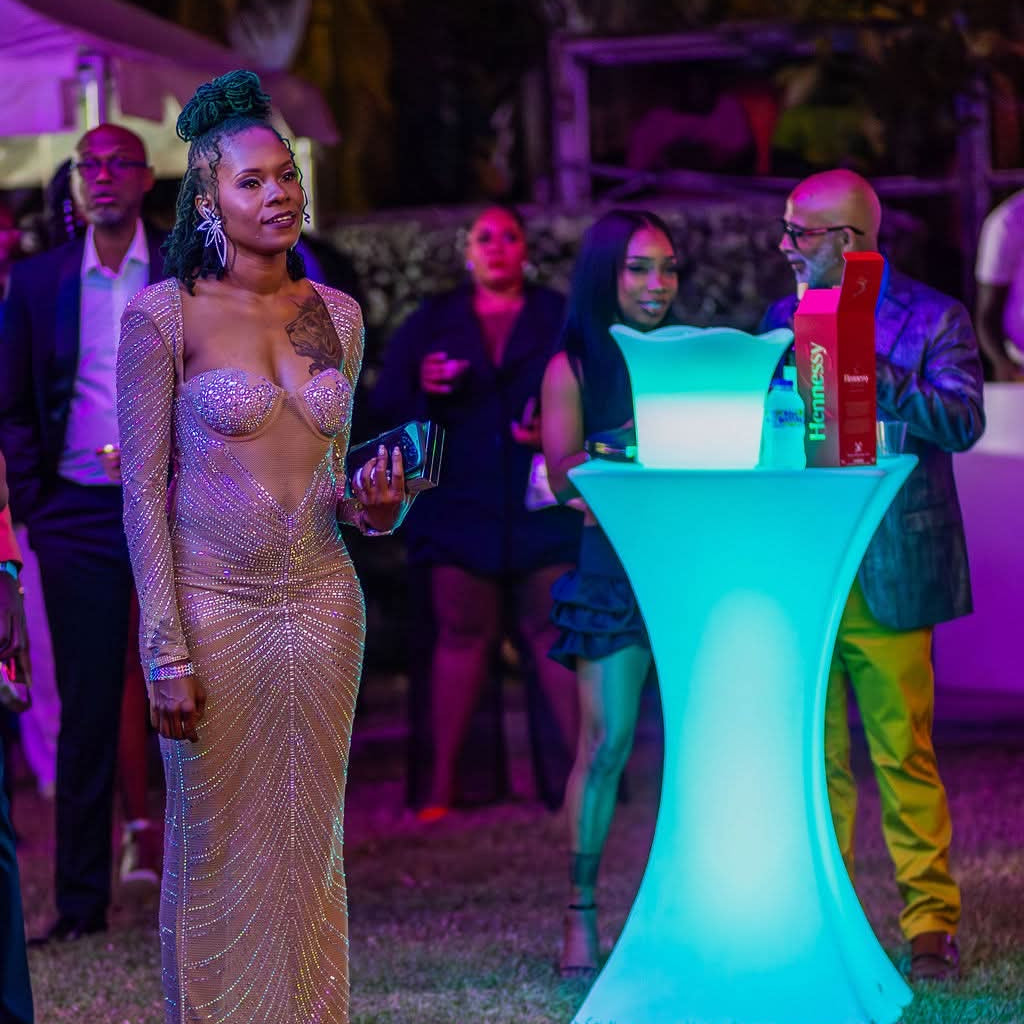 Woman in a sparkly dress standing next to a glowing blue table with people in the background.